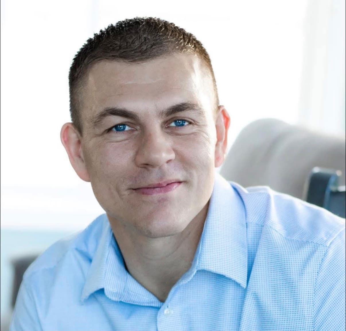 Professional headshot of the founder, in a light-blue shirt
